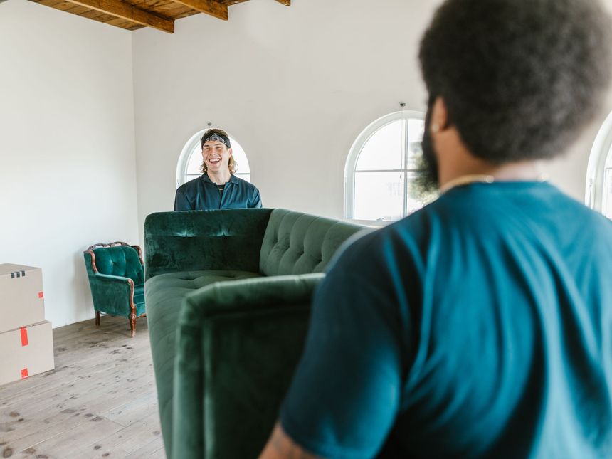 Zwei Träger tragen ein Sofa in eine helle Wohnung mit Umzugskartons
