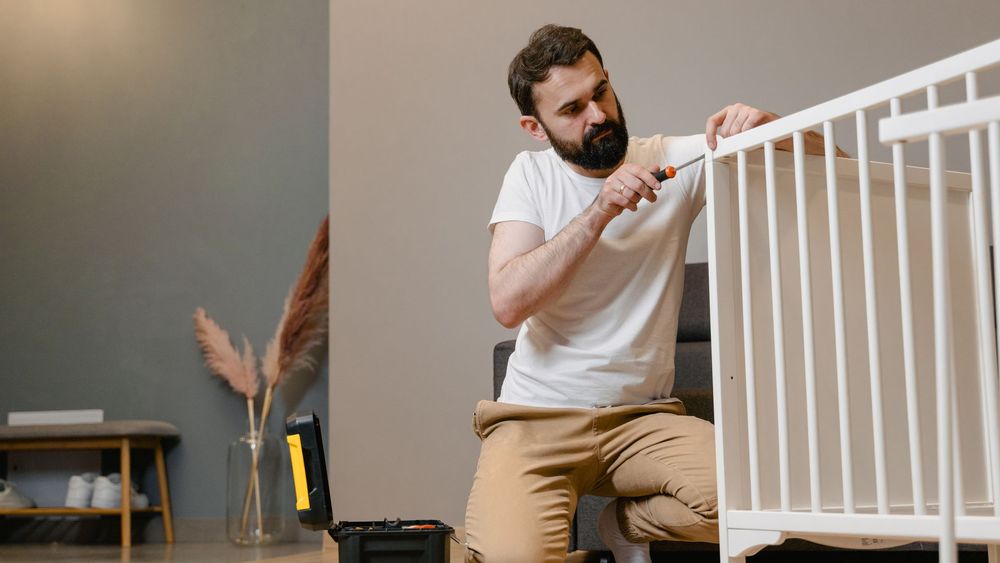 Monteur löst mit einem Akkuschrauber die Verbindungsbeschläge eines Schranks in einem leeren Zimmer