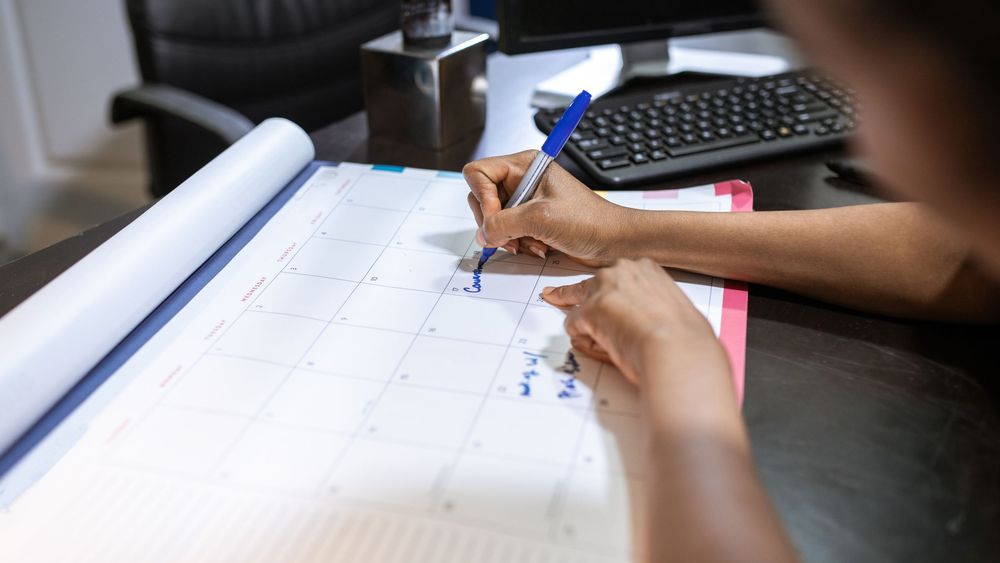 Person notiert eine Umzugsliste neben halb gepackten Kartons und einem geöffneten Kalender