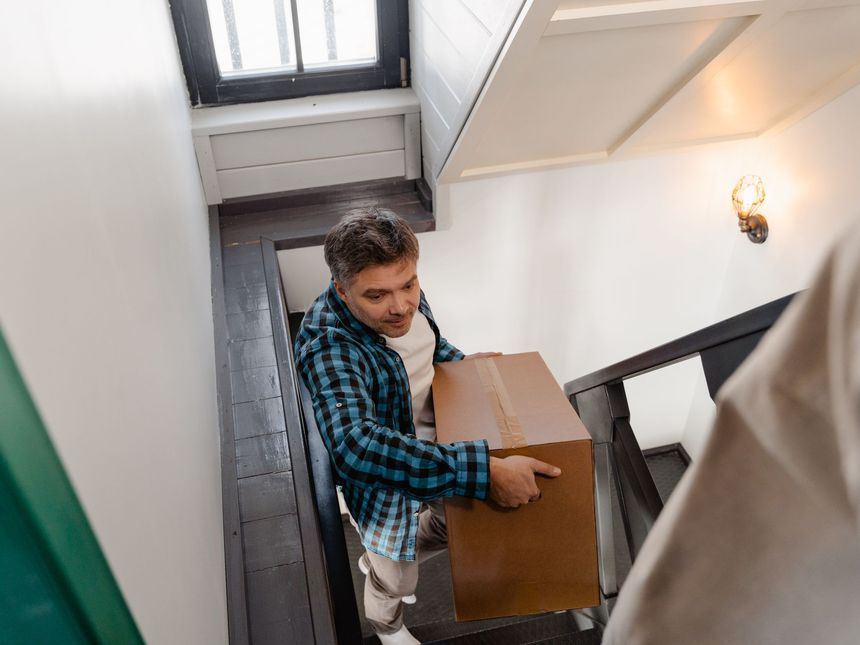 Umzugshelfer tragen einen verpackten Schrank durch ein Treppenhaus